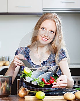 Smiling blonde woman cooking lubina in frying pan photo