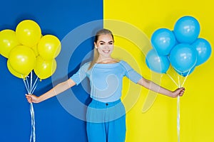 Smiling blonde woman holding blue and yellow balloons on blue