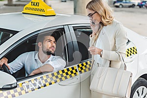 smiling blonde woman talking by smartphone and looking at male driver sitting