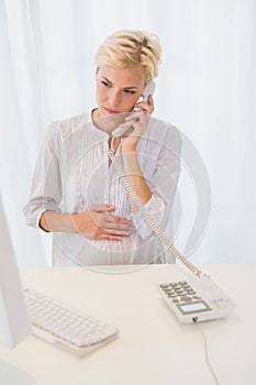 Smiling blonde woman using computer and phoning