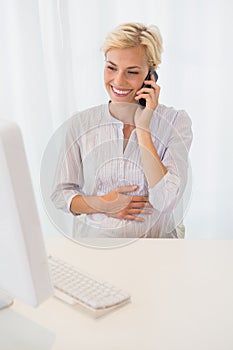 Smiling blonde woman using computer and phoning