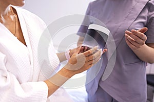 Smiling blonde woman in white coat with paper catalog in her hands consults with her beautician