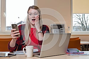 Smiling blonde woman, who is sitting at a laptop and surprised l