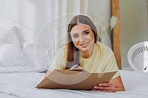 Woman writes in paper notebook with bionic arm lying on bed