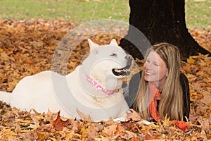 Smiling Blonde Women and White Dog Lying in Autumn Leaves