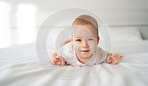 Smiling blue-eyed baby girl four months old lying on the bed looking at the camera, baby care, toodler in the bedroom at