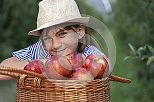 Smiling Blue Eyed Girl in a Straw Hat With A Basket of Red Apples