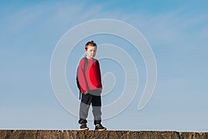 Smiling boy with a backpack behind his back against the sky. Back to school. The boy raised his hands up. Happy student