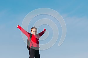 Smiling boy with a backpack behind his back against the sky. Back to school. The boy raised his hands up. Happy student