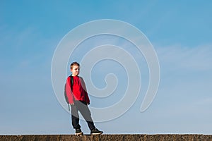 Smiling boy with a backpack behind his back against the sky. Back to school. The boy raised his hands up. Happy student