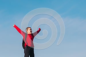 Smiling boy with a backpack behind his back against the sky. Back to school. The boy raised his hands up. Happy student