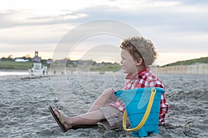 Smiling Boy on Beach with Blue Pail at Sunset