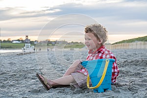 Smiling Boy on Beach with Blue Pail at Sunset