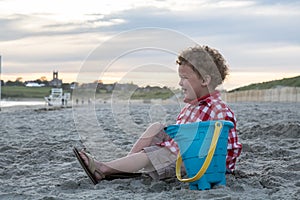 Smiling Boy on Beach with Blue Pail at Sunset