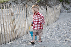 Smiling Boy on Beach with Blue Pail at Sunset