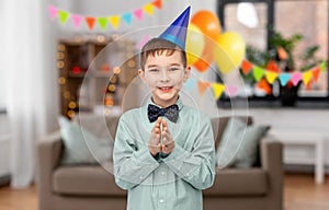 smiling boy in birthday party hat clapping hands