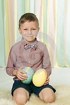 The smiling boy with a bow tie sitting on the floor with the easter eggs in his hands