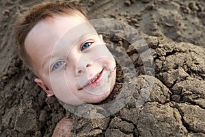 Smiling boy buried in sand on beach