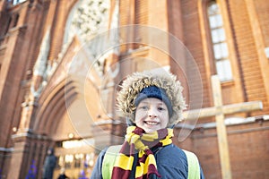 a smiling boy, a child in warm winter clothes, stands near the Catholic Church.