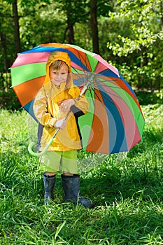 smiling boy with colorful umbrellà stands on lawn