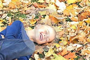 Smiling boy dabbles in autumn Park is laying on leaves in the fall