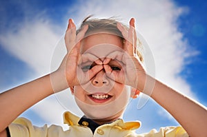 Smiling boy did fingers like binoculars and looks through them