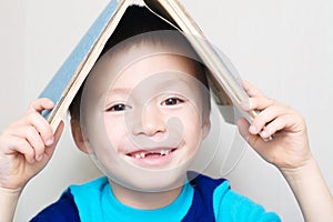 Smiling boy with dropped milk tooth with book on head making roo