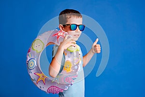 smiling boy enjoy swimming pool with thumb up wearing blue T-shirt on light blue studio background