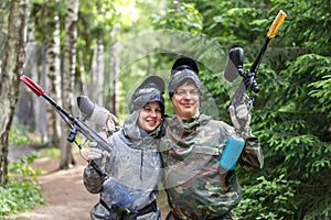 Smiling boy and girl posing with paintball markers outdoors