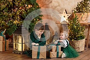 Smiling boy and girl with present gift box sitting near stylish decorated Christmas tree.