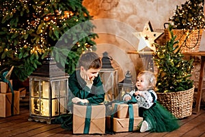 Smiling boy and girl with present gift box sitting near stylish decorated Christmas tree.