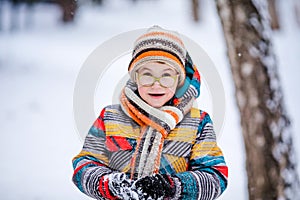 Smiling boy with green big glasses, knitting hat and scarf. Winter snowy background