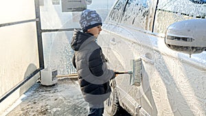 Smiling boy helping washing car with brush and foam. Concept of parenting, children helping parents and automobile care