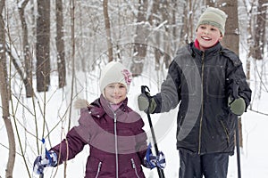 Smiling boy and his sister stand with ski poles