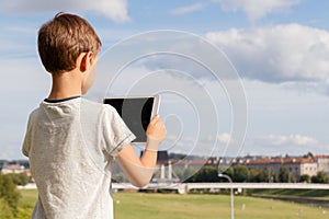 Smiling boy hold tablet PC. Outdoor. Blue sky and city background. Back to school, education, learning, technology