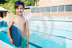 Smiling boy holding kickboard at poolside