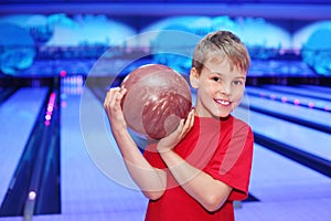 Smiling boy holds ball in bowling club