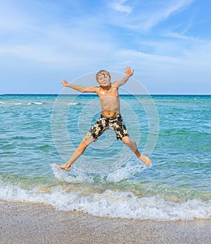 Smiling Boy is jumping in the air at a tropical beach