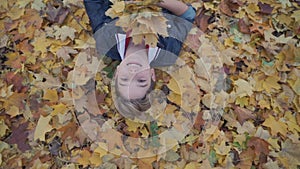 Smiling boy lies on yellow leaves in autumn forest