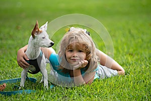 Smiling boy lying on grass with doggy. Happy child playing with dog on lawn.