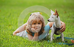 Smiling boy lying on grass with doggy. Happy child playing with dog on lawn.