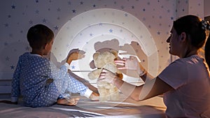 Smiling boy with mother showing theater of shadows with flashlight on the wall. Family having time together, parenting, happy