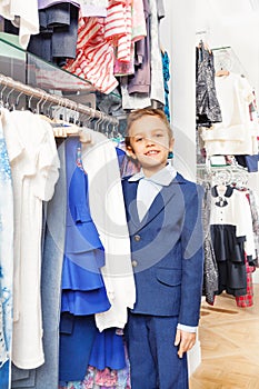 Smiling boy in navy suit standing near clothes