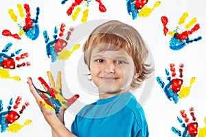 Smiling boy with painted hands on background of hand prints