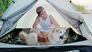 Smiling boy petting Akita Inu while sitting in the tent on the beach