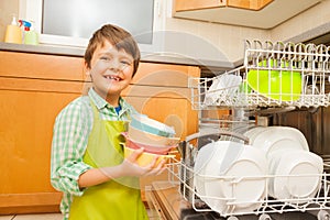 Smiling boy pulling out bowls of the dishwasher photo
