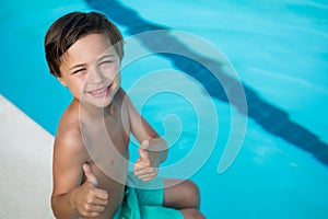 Smiling boy showing thumbs up at poolside