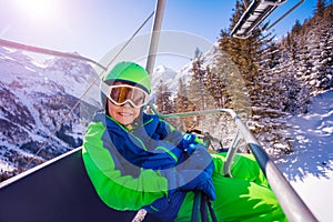 Smiling boy sit on the ski chair lift over forest