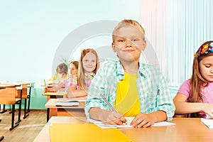 Smiling boy sits in class and holds pen to write