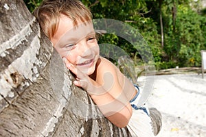 Smiling boy sitting on palm tree